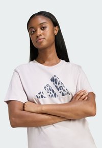 Světlé růžové tričko s texturovaným leopardím potiskem loga Adidas. Krátké rukávy, kulatý výstřih, měkká bavlněná látka a volný střih.