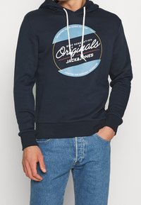 Marinblå hoodie med en cirkulär grafik med texten "Jack & Jones". Tillverkad av mjukt tyg, med ribbade ärmslut och känguruficka.