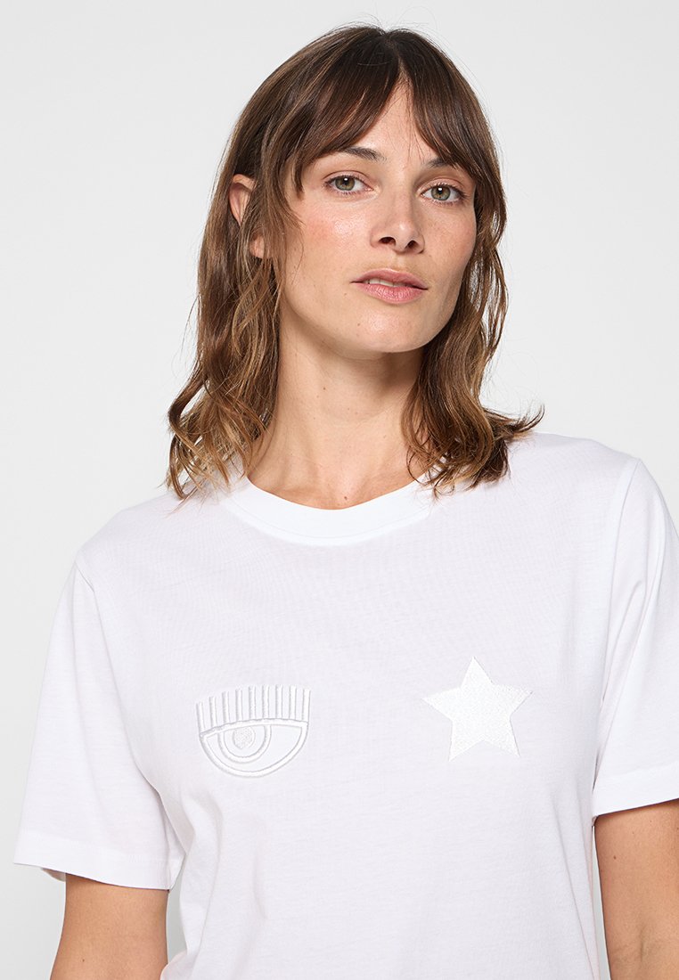 T-shirt blanc à manches courtes avec des motifs brodés en relief d'un œil et d'une étoile sur le devant. Fabriqué en coton doux et respirant.
