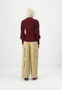 Maroon ribbed sweater with puff sleeves, paired with beige cargo pants featuring multiple pockets and a relaxed fit. Black footwear visible.