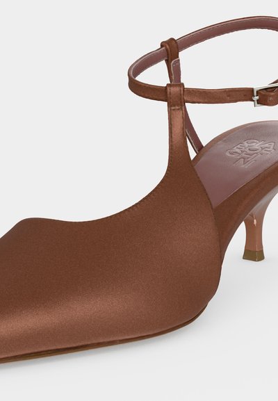 Καφέ σατέν παπούτσι με μυτερή μύτη, λεπτό λουράκι στον αστράγαλο, μικρό τακούνι τύπου kitten και ανάγλυφο λογότυπο στην πέλμα.