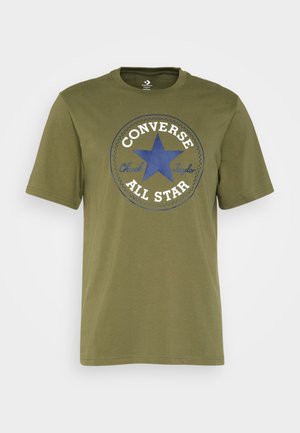Zielona koszulka z krótkim rękawem z niebieską gwiazdą i białym logo "Converse All Star Chuck Taylor" nadrukowanym z przodu.