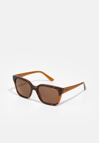 Schildpatt-Sonnenbrille mit braunen Gläsern, quadratischem Design und transparenten Bügeln. Mit "vogue"-Logo an den Schläfen.