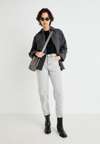 Casaco oversized cinza, suéter preto curto, jeans claros de cintura alta e botas de tornozelo pretas. Os acessórios incluem óculos de sol pequenos pretos e uma bolsa transversal cinza.
