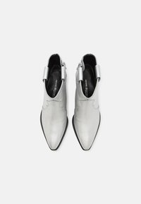 Botines plateados hechos de cuero metálico con punta afilada y diseño con volantes, que presentan una cremallera lateral y una suela negra texturizada.