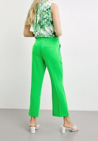 Jasnozielone, szerokie spodnie z gładkiego materiału. Posiadają tylne kieszenie i dopasowany krój. Noszone z bluzką w kwiatowy wzór i białymi obcasami.