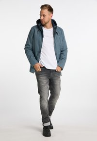 Blå vattentät jacka med huva, grå jeans och svarta skor. Jackan har dragkedja och knappstängning med två framfickor.