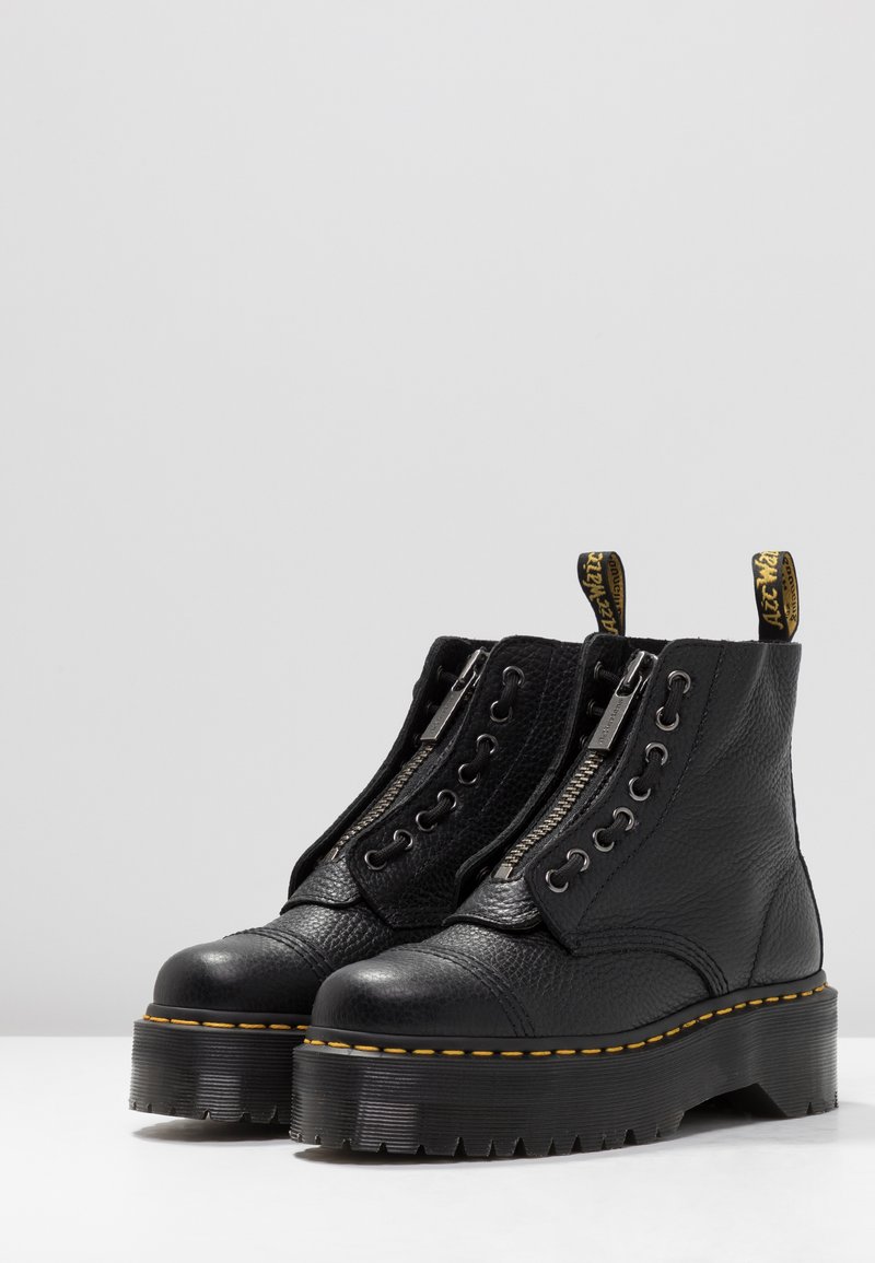 Black leather ankle boots featuring a textured finish, dual zippers, lace accents, and a chunky platform sole with yellow stitching.