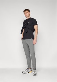 Black T-shirt with text, light grey pants, and grey sneakers with orange and black accents. Model stands confidently against a plain background.