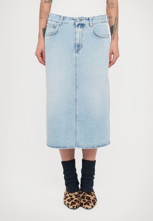 Jupe midi en denim bleu clair à coupe droite, fermeture éclair et bouton, avec poches avant ; portée avec des chaussettes texturées foncées et des chaussures à imprimé léopard.
