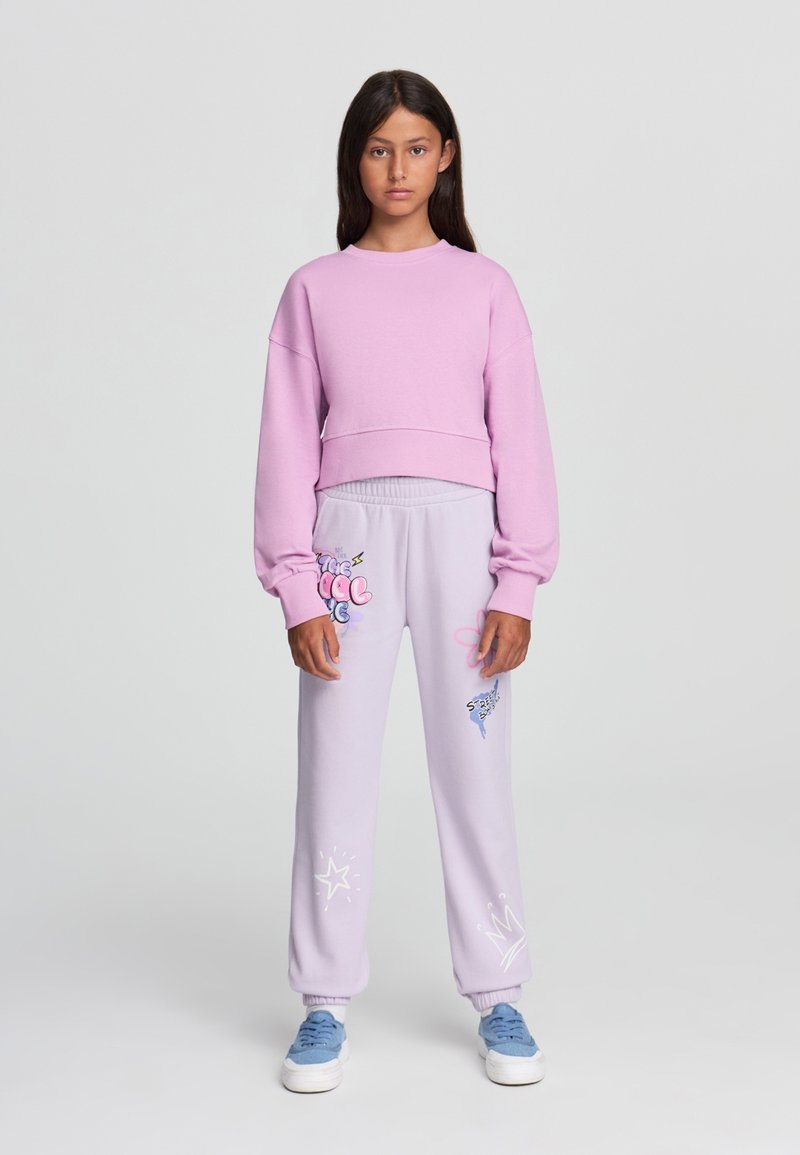Sweatshirt cropped di un rosa chiaro con maniche lunghe e scollatura rotonda, abbinato a pantaloni felpa lilac con stampe colorate e orli a costine.