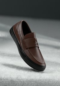 Pantof de piele maro, slip-on, cu o curea căptușită care are un detaliu în formă de stea, talpă din cauciuc negru și accente texturate pe laterale.