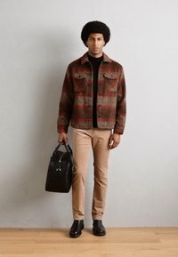 Geruite wollen jas in bruin en rode tinten, zwarte trui, camelkleurige broek, zwarte handtas en zwarte laarzen, met twee borstzakken.