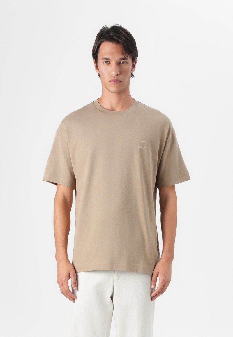 Beige bomulds t-shirt med rund halsudskæring og korte ærmer. Har et lille logo på venstre side af brystet. Glat tekstur, afslappet pasform.