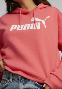 Sudadera de color rosa coral con el logotipo "PUMA" en blanco y emblema gráfico de un gato. Tejido suave con cordones ajustables y mangas acampanadas.