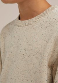 Ljusbeige tröja med rund halsringning, med flerfärgade prickar i brunt och blått, samt en ribbad krage.