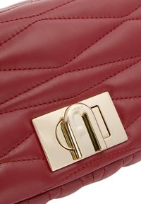 Borsa a manico in pelle rossa con motivo trapuntato, dotata di dettagli in metallo dorato e chiusura con logo. Texture liscia con dettagli di cucitura a contrasto.