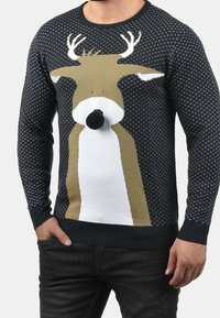 Jersey de punto con un diseño de reno en marrón y blanco sobre un fondo azul marino, con patrones texturizados y puños y dobladillo acanalados.