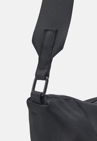 Černá látková taška přes rameno s texturovaným povrchem, vybavená odolným popruhem a kovovými prvky pro upevnění. Sofistikované designové prvky.