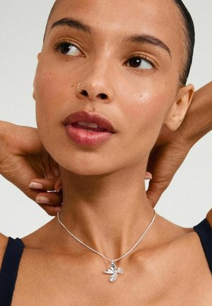 Silverhalsband med ett blommigt hänge som har flera bladformer och en klar ädelsten. Bärs på en slät hud med en mörk topp.