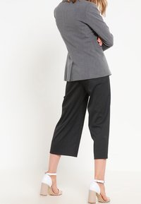 Šedý blazer s přiléhavým střihem, doplněný o černé zkrácené kalhoty. Obuv má bílé pásky a béžové blokové podpatky.