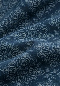 Námořnická modrá látka s propracovanými světle modrými květinovými a scrollovými vzory, která se vyznačuje texturovanou tkaninou, jež dodává hloubku a rozměr.