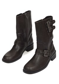 Botines de cuero marrón con textura suave, cremallera lateral y detalles de hebilla en el eje. Diseño de tacón cuadrado y punta redondeada.