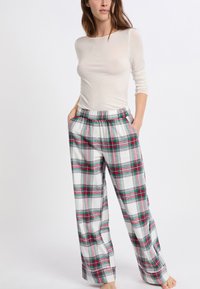 Witte langemouwen top gecombineerd met wijde gestreepte broek in plaid met rode, groene en zwarte lijnen op een witte achtergrond. De broek heeft zakken.