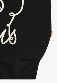 Black knitted sweater featuring cream-colored text design. Ribbed hem and a small branded tag on the side. Smooth texture throughout.