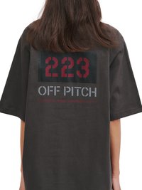 Person mit schulterlangen Haaren trägt ein schwarzes T-Shirt mit roter "223" und grauem "OFF PITCH" Text auf dem Rücken.