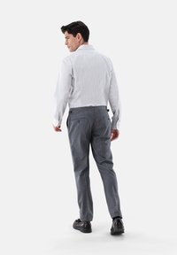 Weiß gestreifte Hemdbluse mit langen Ärmeln und grauen Hosen, die eine taillierte Passform und Gesäßtaschen aufweisen. Schwarze Schuhe runden das Outfit ab.