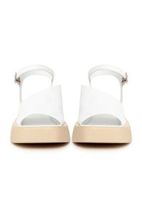 Paire de sandales blanches à bout ouvert avec larges brides à l'avant, brides de cheville avec boucles et semelles rembourrées beiges, vues de face.