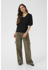 Schwarzes kurzärmeliges Oberteil mit rundem Ausschnitt, kombiniert mit weiten olivgrünen Cargo-Hosen mit Seitentaschen und Reißverschlusstaschen. Schwarze Slipper.