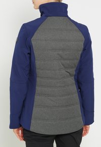 Mörkblå jacka med en figursydd design, med en grå vadderad rygg, hög krage och slät textur på ärmar och bål.