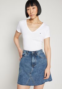 Hvit tettsittende t-skjorte med V-hals og korte ermer, kombinert med et blått denim miniskjørt med fransk kant og skrå sømdetaljer.