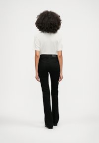 Calças de ganga pretas à boca de sino com uma silhueta ajustada, combinadas com uma t-shirt branca de mangas curtas. O conjunto apresenta uma textura suave e um design básico.