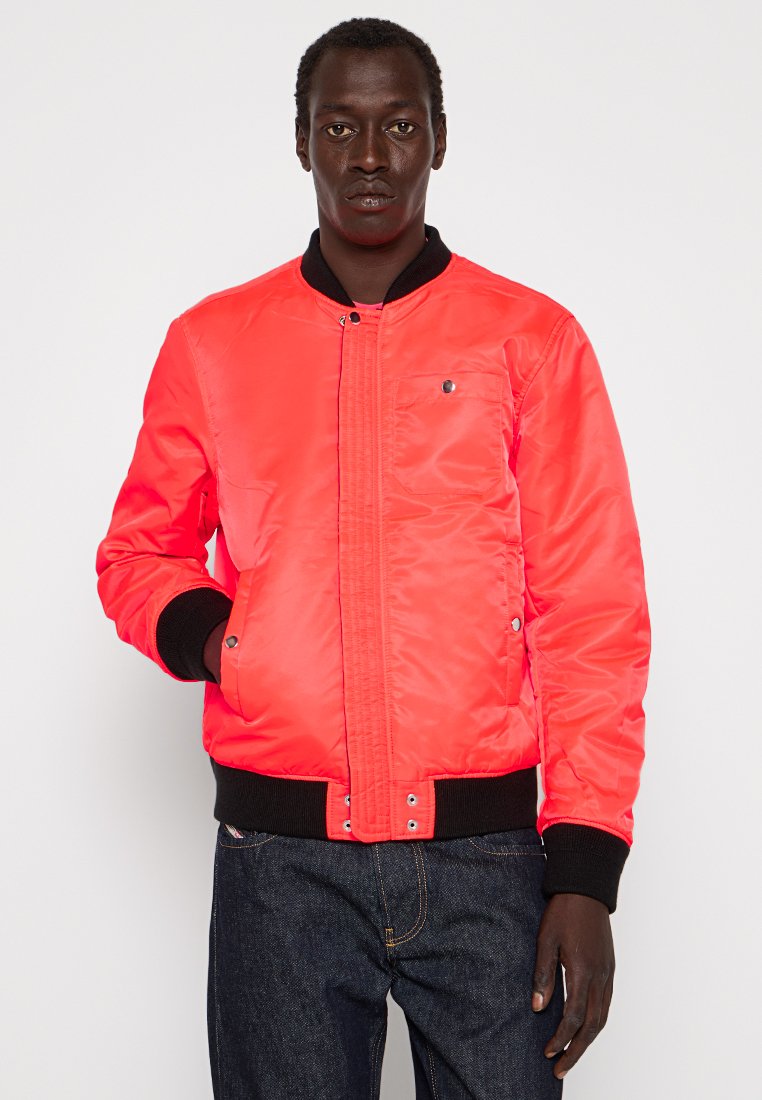 Veste bomber en satin rouge avec fermeture éclair, poignets et col côtelés, dotée d'une poche poitrine et de deux poches latérales. Accents noirs sur les ourlets.