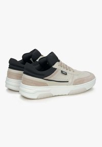 Beige suède en zwarte synthetische sneakers met een dikke witte zool, voorzien van perforaties aan de zijkanten en veters aan de voorkant.