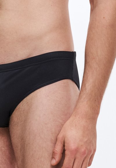 Cuecas de banho pretas com textura suave, design de cintura baixa e detalhes mínimos de costura, ajustadas ao corpo para conforto e suporte.