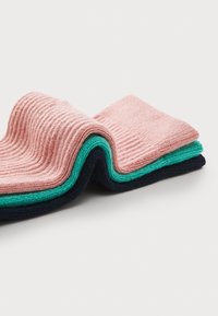 Quatre paires de chaussettes côtelées en rose, teal et marine, empilées ensemble, mettant en valeur la texture du matériau et la variation des couleurs.