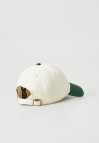 Katoenen pet met een witte body en groene klep. Bevat een groene knop bovenop en een verstelbare band aan de achterkant met een logo-tag.
