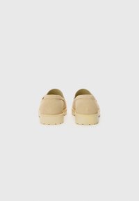 Beige Wildlederschuhe mit runder Kappe, minimaler Naht und dickem, cremefarbenem Gummisohle, die eine klassische Rückansicht zeigt.