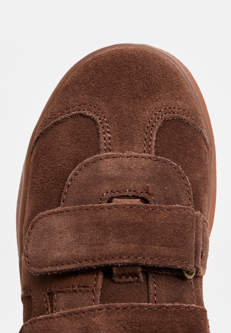 Braune Wildlederschuhe mit einem Klettverschluss, runder Spitze und gesteppten Akzenten. Die strukturierte Oberfläche verbessert den Halt und den Komfort.