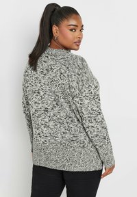 Grå och svart prickig stickad tröja med avslappnad passform, långa ärmar och ribbade manschetter. Har en något förlängd nederkant bak.