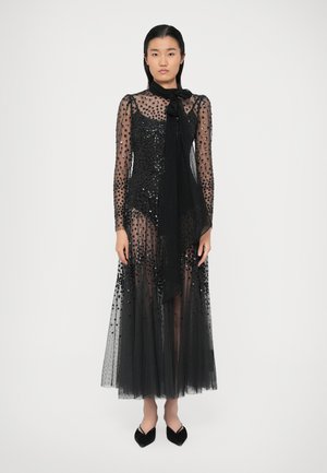 Schwarzes Kleid aus einem transparenten, gepunkteten Stoff mit Pailletten, langen Ärmeln und einem Schleifen-Detail am Hals. Bodenlanger Tüllrock.