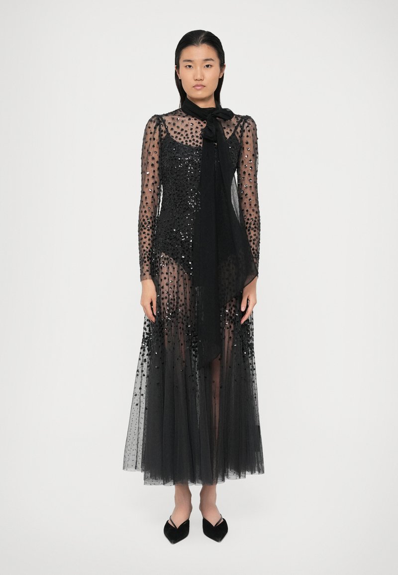 Mustläid, millel on läbipaistev, täpikujuline kangas, millel on sädelevad detailid, pikad varrukad ja kaelal lips. Põrandani ulatuv tülli seelik.