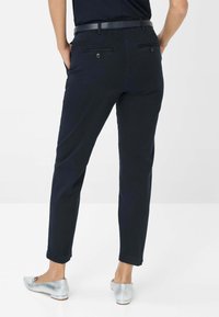 Pantaloni blu navy con taglio dritto, dotati di due tasche posteriori e una cintura nera. Abbinati a ballerine argentate lucide.