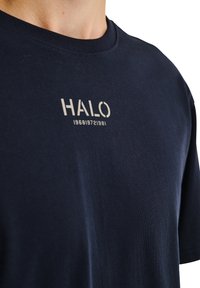 Marinblå bomulls-T-shirt med rund hals och ett grafiskt tryck med texten "HALO 196819721981" i ljusgrått på framsidan.