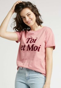 T-shirt en coton rose à manches courtes avec le texte "Toi et Moi" en bordeaux foncé. Coupe décontractée avec un col rond et une texture douce.