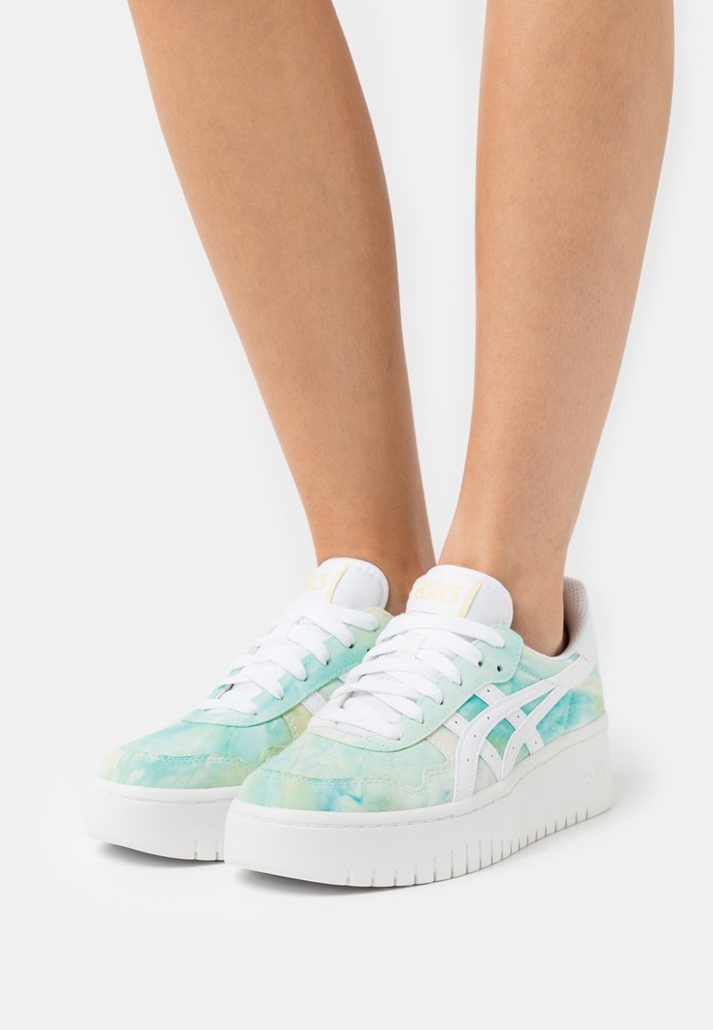 Baskets tie-dye bleu clair et vert avec des accents blancs, semelle surélevée et lacets blancs. Marquage sur la languette et le côté. Tissu confortable.